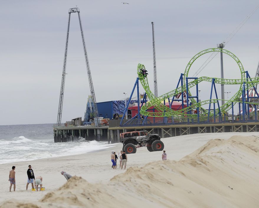 In this May 20, 2017, photo, people enjoy beachside games as a a wagon from the Hydrus roller coaster, top right, goes over a turn at Casino Pier in Seaside Heights, N.J. More than four years after Superstorm Sandy destroyed part of the Casino Pier and left the since-demolished Jet Star roller coaster partially submerged in the Atlantic Ocean, the new roller coaster named Hydrus opened May 6, 2017, built safely inland above the beach rather than out over the water. (AP Photo/Julio Cortez)