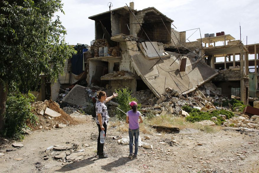 In this May 18, 2017 photo, Adibeh Ghosn and her daughter Samar look to their destroyed house at the mountain resort town of Zabadani in the Damascus countryside, Syria. Once a popular summer resort famed for its fruit trees and favored by tourists from rich Gulf Arab countries, Zabadani is now a deserted, endless vista of pulverized buildings after thousands of rebels were driven out along with the town's original inhabitants. (AP Photo/Hassan Ammar)