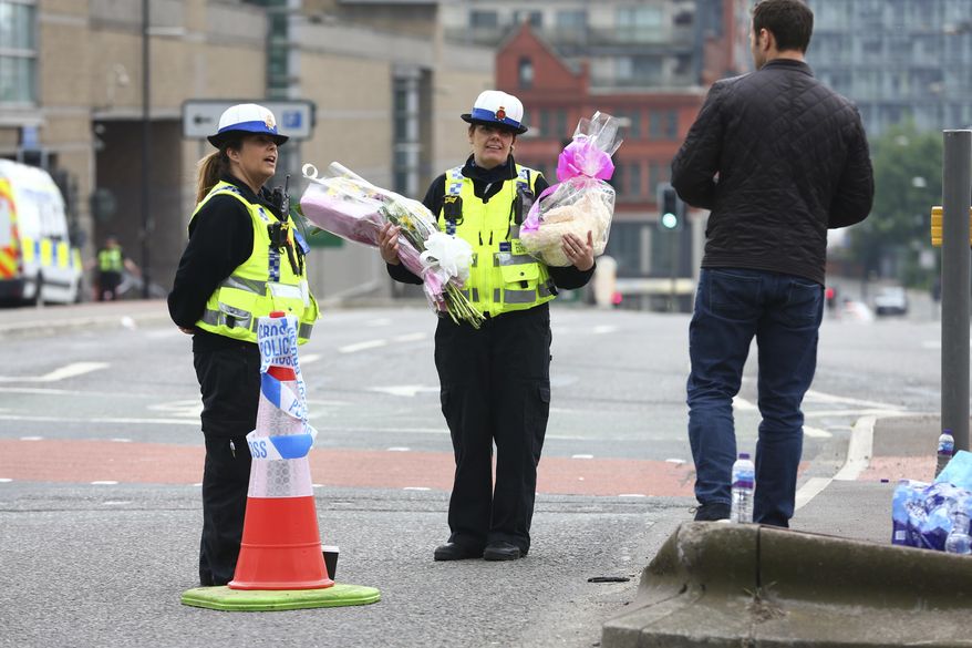 A police officer accepts tributes from a man outside the Manchester Arena in Manchester, England, Wednesday, May 24, 2017. Britons will find armed troops at vital locations Wednesday after the official threat level was raised to its highest point following a suicide bombing that killed more than 20, as new details emerged about the bomber. (AP Photo/Dave Thompson)