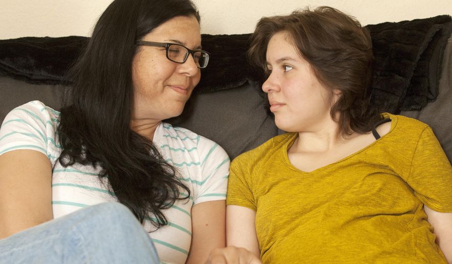 In this May 23, 2017 photo, Laura Polanco and daughter, Meredith Erck comfort each other while recalling months of fighting Erck's brain tumor while she tried to complete her high school course work in Rapid City, S.D. Erck is six credits short of earning her Rapid City Central high school diploma, and although she will finish them over the summer, is not being allowed to participate in the graduation ceremony with her twin brother, Martin. (Hannah Hunsinger/Rapid City Journal via AP)