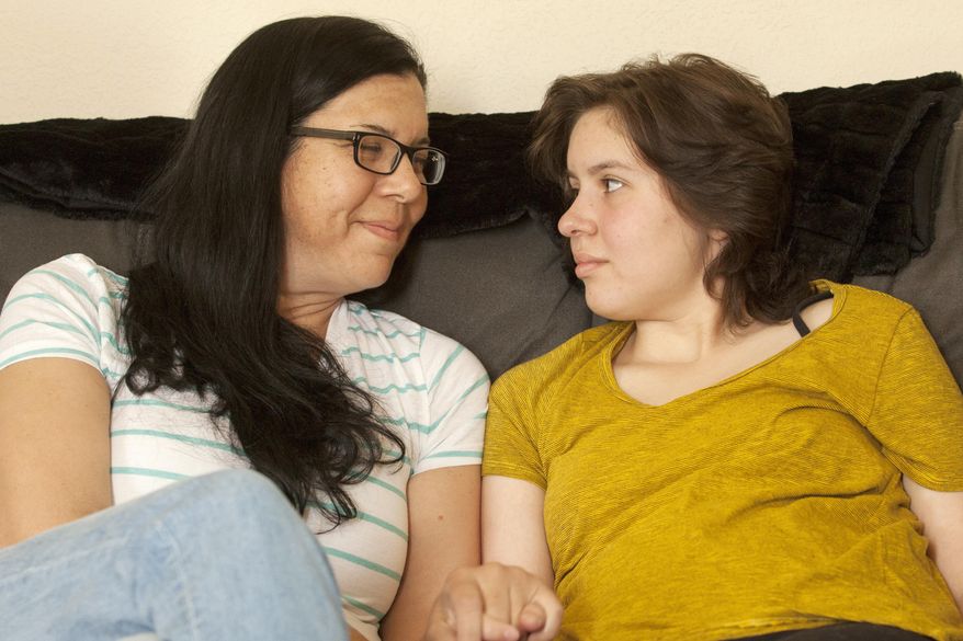 In this May 23, 2017 photo, Laura Polanco and daughter, Meredith Erck comfort each other while recalling months of fighting Erck's brain tumor while she tried to complete her high school course work in Rapid City, S.D. Erck is six credits short of earning her Rapid City Central high school diploma, and although she will finish them over the summer, is not being allowed to participate in the graduation ceremony with her twin brother, Martin. (Hannah Hunsinger/Rapid City Journal via AP)