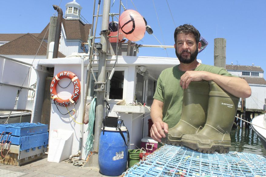 In this May 19, 2017 photo, John Aldridge poses in Montauk, N.Y. with the boots that helped keep him afloat for 12 hours after falling off his lobster boat in the summer of 2013. Nearly four years later, he's still working in the profession that put him in so much danger. And he's retelling the remarkable tale in a book released the week of May 29, 2017. (AP Photo/Frank Eltman)
