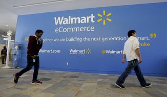 FILE - In this Wednesday, Sept. 18, 2013, file photo, two Wal-Mart employees walk past a sign in the lobby at the Walmart.com office in San Bruno, Calif. Wal-Mart’s acquisition of Jet.com is accelerating its progress in e-commerce as it works to narrow the gap between itself and online leader Amazon. Wal-Mart is betting its online future on essentials like produce and groceries and has adjusted its shipping strategy. But Amazon keeps innovating too. (AP Photo/Jeff Chiu, File)