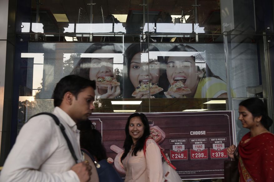 In this Monday, May 29, 2017 photo, commuters walk past a fast food restaurant in New Delhi, India. More than two decades of rapid economic growth has changed Indians’ lifestyles. People eat out more often, and prefer Western-style junk food such as burgers and pizza over traditional lentil and vegetable meals. The changes have brought a sharp rise in obesity, along with lifestyle diseases such as diabetes, even as India still has some of the world’s worst levels of malnourishment and stunted childhood growth due to a paucity of food. (AP Photo/Tsering Topgyal)