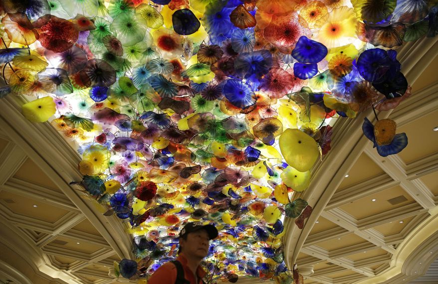 In this May 31, 2017, photo, a man stands beneath an installation by artist Dale Chihuly titled, "Fiori di Como," (Flowers of Como), suspended from the ceiling of the lobby at the Bellagio hotel and casino in Las Vegas. Chihuly, who began working with glass in the 1960s, is a pioneer of the glass art movement. Known for styles that include vibrant seashell-like shapes, baskets, chandeliers and ambitious installations that can be seen in botanical gardens, hotels and the new Chihuly Sanctuary at the Buffett Cancer Center in Omaha, Neb. (AP Photo/John Locher)