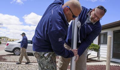 In this Thursday, May 18, 2017 photo, Brantley Cargill and Jamie Popwell, right, of Flags for Vets erect a new flag pole in the front yard of Medal of Honor recipient Hiroshi Miyamura in Gallup, N.M. Gallup neighbors can now recognize the house of Miyamura by the new flag pole erected in front of his house. The Flag for Vets organization installed Miyamura’s new flag with lights so he won’t have to take it down each day. (Cable Hoover/Gallup Independent via AP)