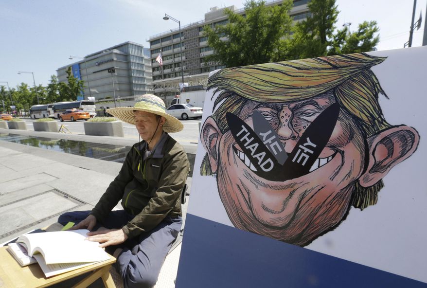 A South Korean protester sits next to a poster with an illustration of U.S. President Donald Trump to oppose a plan to deploy an advanced U.S. missile defense system called Terminal High-Altitude Area Defense, or THAAD, near the U.S. Embassy in Seoul Monday, June 5, 2017. South Korea's presidential office says a senior defense official has been suspended for deliberately failing to report the arrival of several more launchers for a contentious U.S. missile defense system meant to deal with North Korean threats. (AP Photo/Ahn Young-joon)