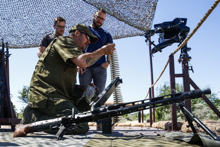 ADVANCE FOR USE MONDAY, JUNE 12, 2017, AND THEREAFTER - In this May 24, 2017, photo, Glenn Fleming, center, loads up an MG-42 machine gun for guests participating in an Allies and Axis all-day experience at Ox Ranch in Uvalde, Texas. The ranch is a free-roaming range filled with exotic animals, some to hunt, and home to DriveTanks.com, where tourists pay to transport themselves into another era and another life. (Michael Ciaglo/Houston Chronicle via AP)