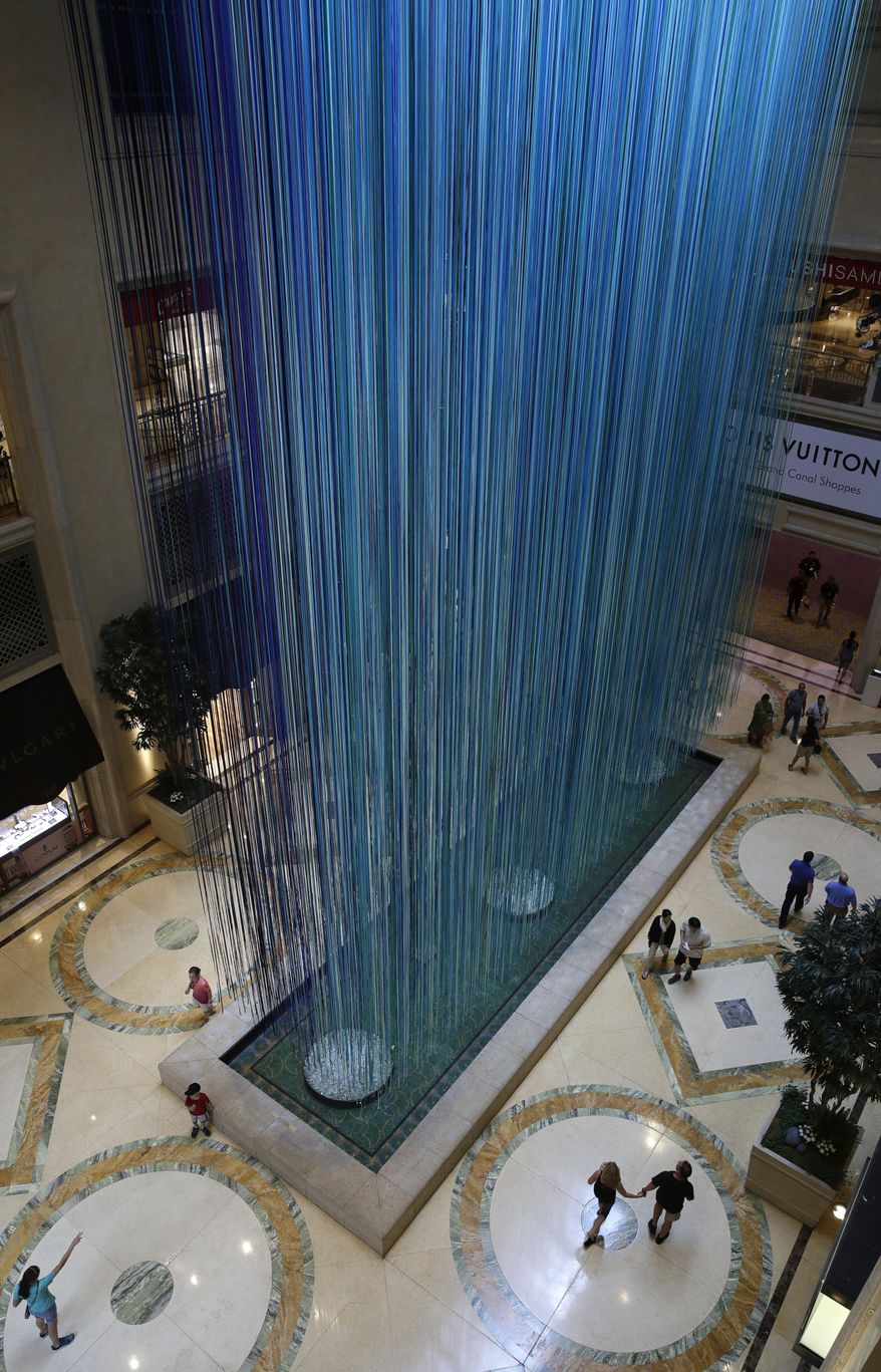 People walk by an art installation titled "Another Sky" by artist Anne Patterson, Thursday, June 8, 2017, in Las Vegas. The installation, at the Palazzo hotel and casino, consists of around 3500 ribbons suspended from the ceiling. (AP Photo/John Locher)