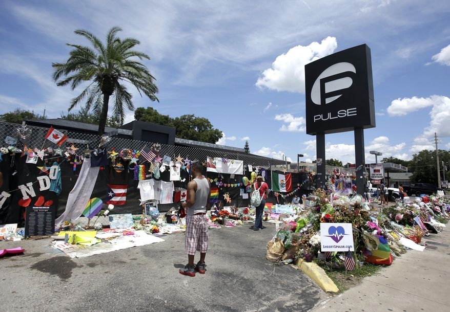 FILE - In this July 11, 2016, file photo, visitors gather at a makeshift memorial outside the Pulse nightclub in Orlando, Fla. Church bells will toll throughout the Orlando area as residents reflect on the 49 patrons killed during a massacre at the gay nightclub Pulse in the worst mass shooting in recent U.S. history. Starting in the wee hours Monday, June 12, 2017, and continuing almost 24 hours later, survivors, victims’ families, city officials and central Florida residents will remember the victims with multiple services. (AP Photo/John Raoux, File)