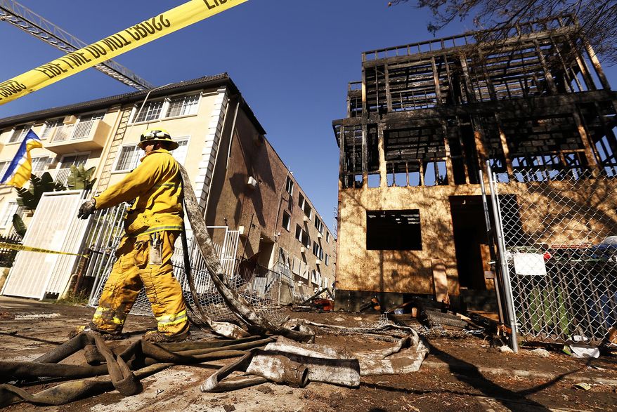 LA City Firefighter Jose Carreon hauling hoses on mop up at the scene in the 400 block of Heliotrope Drive in East Hollywood Monday morning after a fire heavily damaged an apartment building under construction and also damaged an adjacent apartment building, a garage and a house. Firefighters extinguished the flames in about 45 minutes with 1 minor injury to a firefighter. A suspect who may have set the fires is in custody. (Al Seib /Los Angeles Times via AP)