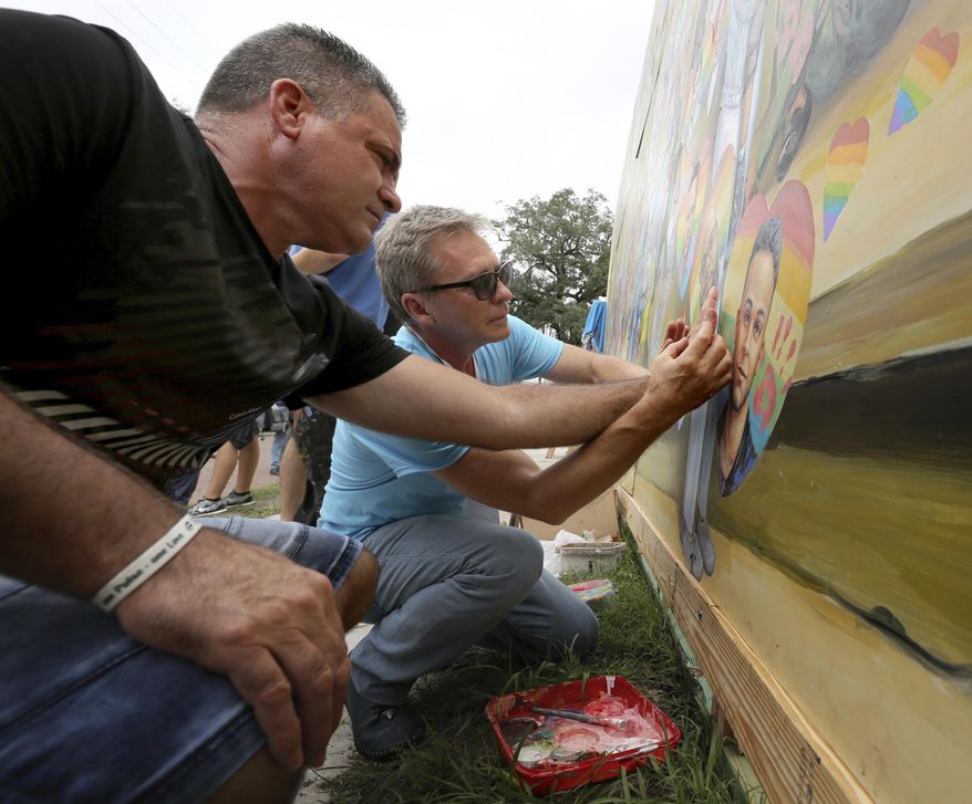 Artist Yuriy Karabash, right, helps Saúl Barrios place a hand print on a mural at the Pulse nightclub, Monday, June 12, 2017, that commemorates the one-year anniversary of the June 12, 2016, massacre that killed 49 at Pulse. Saúl Barrios son, Alejandro Barrios Martínez, was killed in the mass shooting. (Joe Burbank /Orlando Sentinel via AP)