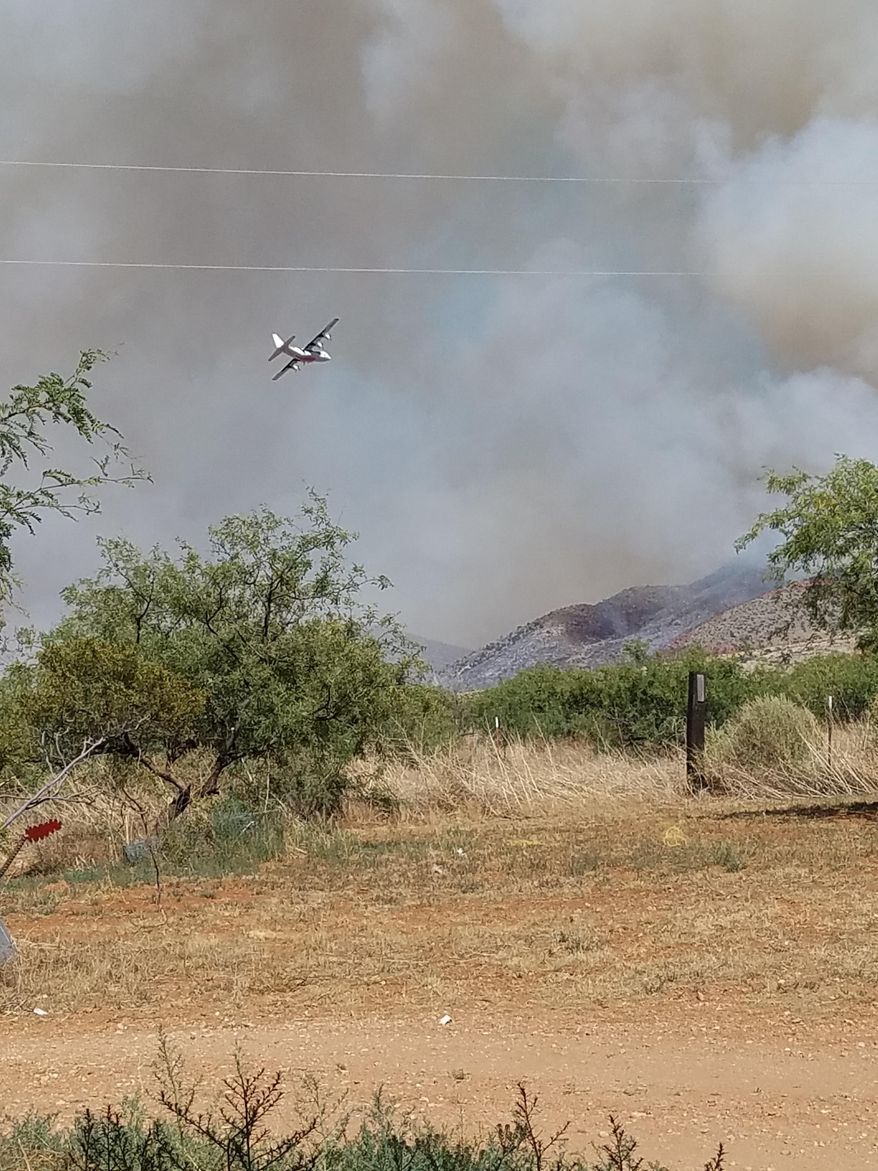 This June 10, 2017 photo provided by Heather Floyd shows a plane flying over the wildfires in Dragoon, Ariz. Nearly 30 wildfires tore through dry and windy Arizona on Monday, June 12, 2017, drawing crews from across the Western United States to the state with the most blazes burning in the nation. (Heather Floyd via AP)