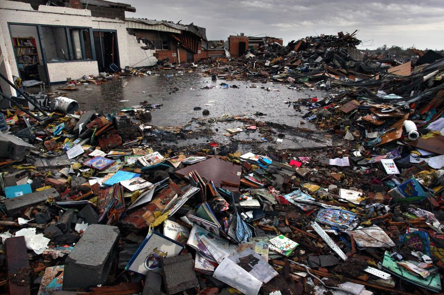 FILE - In this May 23, 2013 file photo, rain falls on the wreckage of Plaza Towers Elementary School, where seven children were killed when a tornado hit Moore, Okla. The Moore public school system has reached an agreement with the families of the seven children ending three years of litigation. Moore Public Schools said Monday, June 12, 2017 that the families have agreed to accept $14,000 each to settle the lawsuit. (AP Photo/Brennan Linsley File)
