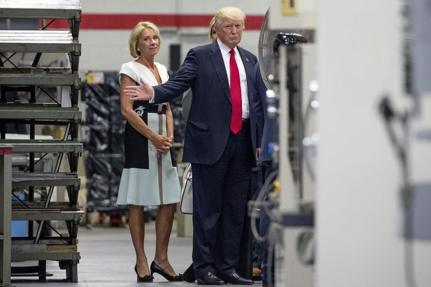 President Donald Trump, accompanied by Education Secretary Betsy DeVos, left, waves to members of the media as he takes a tour of Waukesha County Technical College in Pewaukee, Wis., Tuesday, June 13, 2017. (AP Photo/Andrew Harnik)