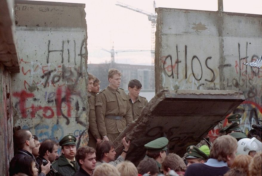 On Nov. 11, 1989, East German border guards are seen through a gap in the Berlin Wall after demonstrators pulled down a segment of the wall at the Brandenburg Gate, Berlin. Associated Press photo