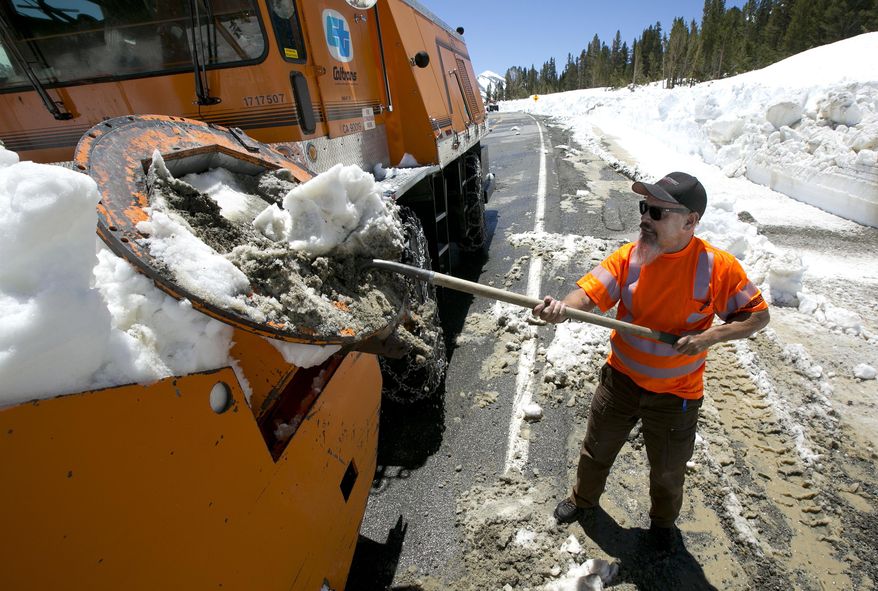 In this photo taken Tuesday, June 6, 2017, Caltrans maintenance worker Paul Jensen removes snow and dirt that is clogging the rotary blower he is operating to clear snow from Highway 120 near near Yosemite National Park, Calif. This year's heavy snowfall has crews working to clear Highway 120 as summer approaches; the only road through Yosemite that connects the Central Valley on the west side with the Owens Valley on the east side of the Sierra Nevada. (AP Photo/Rich Pedroncelli)