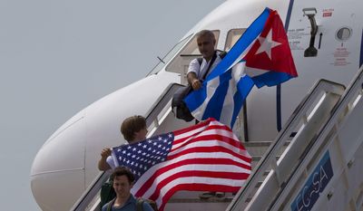 FILE- In this Aug. 31, 2016 file photo, two passengers deplane from JetBlue flight 387 waving a United States, and Cuban national flag, in Santa Clara. As President Donald Trump is expected to announce a reversal on the U.S. Cuba policy on Friday, June 16, 2017, Cubans are bracing for the worst. Across the island, people of all ages, professions and political beliefs expect rising tensions, fewer American visitors and a harder time seeing relatives in the U.S.(AP Photo/Ramon Espinosa, File)