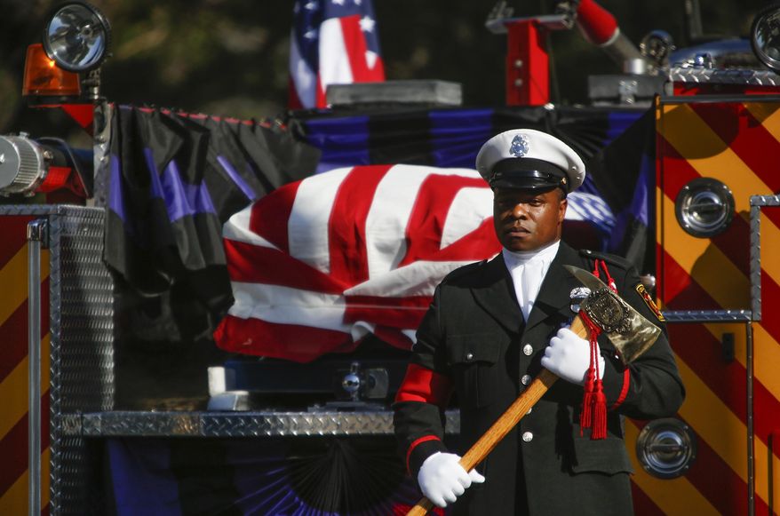 An honor guard stands at attention with an axe at the rear of the fire truck carrying the flag-draped coffin of fallen LAFD Firefighter Kelly Wong at the Cathedral Of Our Lady Of Angels, Friday, June 16, 2017 in Los Angeles. The 29-year-old Wong fell from the ladder on June 3 and died two days later. (Mark Boster /Los Angeles Times via AP)