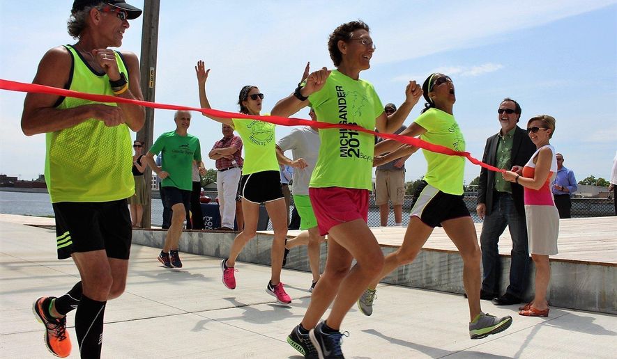 From left, Dan Oemedian, Maureen Pluger and Caroline Cook run through a ceremonial ribbon on the new $1.8 million Coldbrook Edge Trail Thursday, June 15, 2017, in Grand Rapids. The trail runs from Canal Park to Leonard Street along the eastern bank of the Grand River in Grand Rapids. (Amy Biolchini/The Grand Rapids Press via AP)
