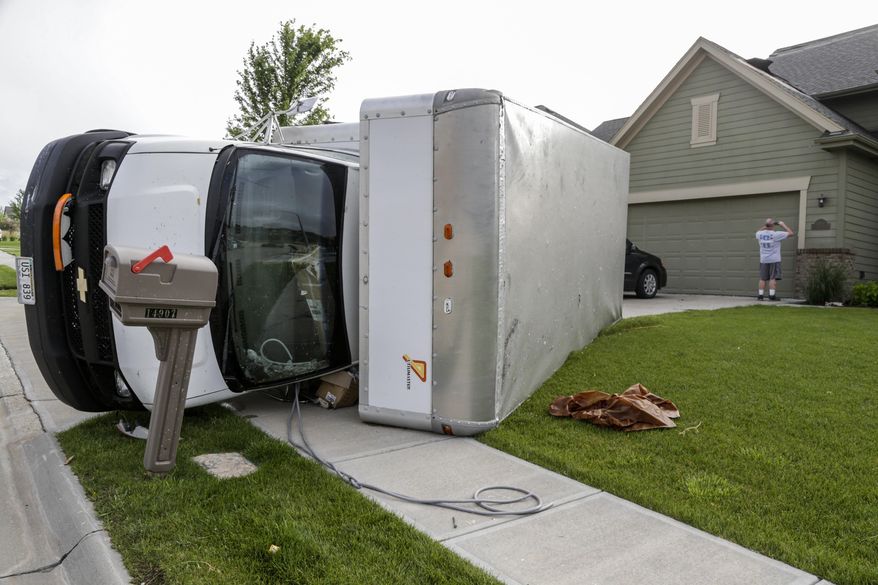 A home owner documents damage to his home as a truck lies on its side in the Hyda Hills neighborhood in Bellevue, Neb., Saturday, June 17, 2017. A severe weather front passed through the area the previous evening. (AP Photo/Nati Harnik)