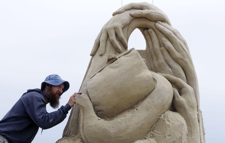 David Andrews, of Wauwatosa, Wisconsin, works on the details of his sand castle titled "Hands of Fate" at the annual sand sculpting classic on Hampton Beach in Hampton, N.H., Friday, June 16, 2017. Artists from New England, Canada, California and Europe compete to create their designs over three days, totaling 24 hours. (AP Photo/Charles Krupa)
