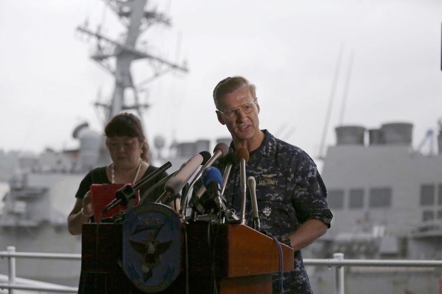 Vice Adm. Joseph Aucoin, right, Commander of the U.S. 7th Fleet, speaks during a press conference near the damaged USS Fitzgerald, rear, at the U.S. Naval base in Yokosuka, southwest of Tokyo Sunday, June 18, 2017. The USS Fitzgerald collided with a container ship in the busy sea off Japan Saturday. (AP Photo/Eugene Hoshiko)