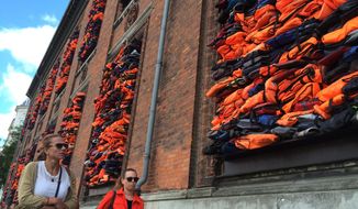 People walk past the new artwork entitled ‘Soleil Levant&#39; (sunrise in French) by Chinese dissident artist Ai Weiwei, made from over 3,500 lifejackets discarded by migrants on the Greek island of Lesbos, following its official inauguration at Copenhagen’s Kunsthal Charlottenborg museum in Copenhagen, Denmark, Tuesday June 20, 2017.  Weiwei has barricaded the windows of the museum for his provocative new artwork as a striking reminder of the ongoing migrant crisis, inaugurated Tuesday on World Refugee Day.  (AP Photo / James Brooks)