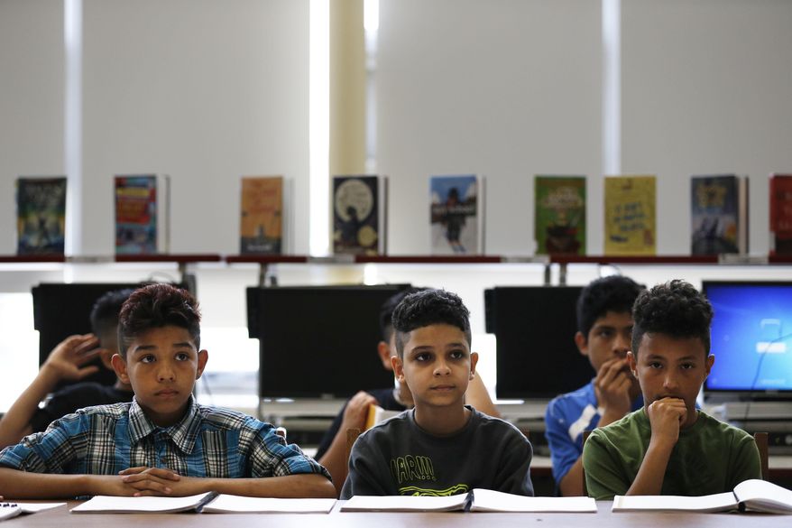 In this Wednesday, June 14, 2017, photo, Jocsan Hernandez, left, and other students of Maria Victoria Mendoza class at Brentwood East Middle school share their sections of "Luchando por un Mejor Futuro" (Fighting for a Better Future), a book they created, in Brentwood, N.Y. A group of young immigrants has written the book about how they fled street gangs in Central America in search of a better life in a New York town now plagued by the same gang violence. (AP Photo/Michael Noble Jr.)