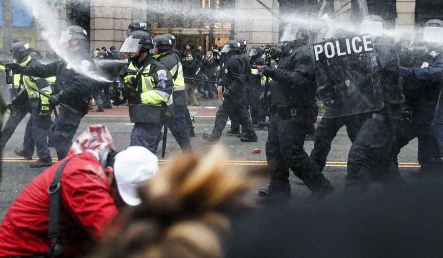 FILE - In this Jan. 20, 2017, file photo, police fire pepper spray at protestors during a demonstration in downtown after the inauguration of President Donald Trump. The American Civil Liberties Union is suing over the actions of District of Columbia police on Inauguration Day. The lawsuit filed June 21, on behalf of four people says police violated their rights by using pepper spray and flash-bang grenades without warning or justification and holding demonstrators without food, water or access to toilets.(AP Photo/John Minchillo, File)