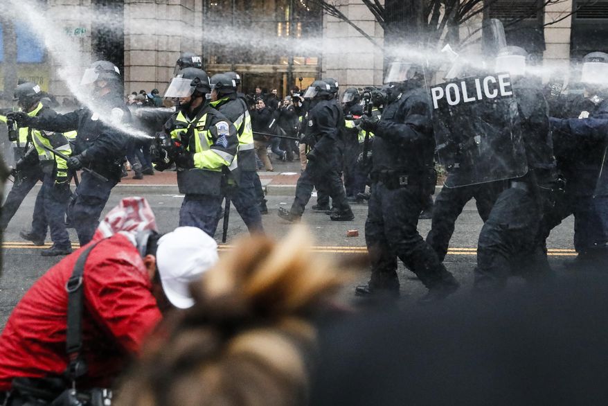 FILE - In this Jan. 20, 2017, file photo, police fire pepper spray at protestors during a demonstration in downtown after the inauguration of President Donald Trump. The American Civil Liberties Union is suing over the actions of District of Columbia police on Inauguration Day. The lawsuit filed June 21, on behalf of four people says police violated their rights by using pepper spray and flash-bang grenades without warning or justification and holding demonstrators without food, water or access to toilets.(AP Photo/John Minchillo, File)