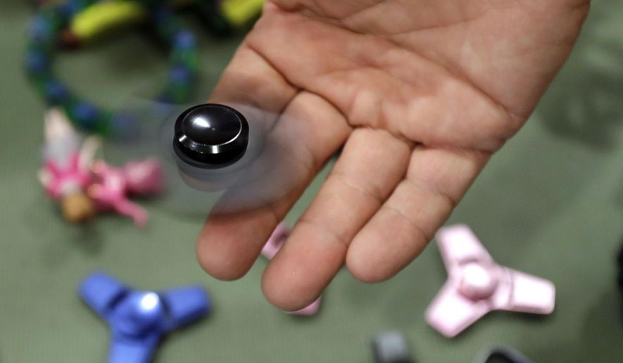 FILE - In this May 11, 2017, file photo, Funky Monkey Toys store owner Tom Jones plays with a fidget spinner in Oxford, Mich. Fidget spinners are among the those on the annual list of hazardous summer toys compiled by World Against Toys Causing Harm, Inc., a nonprofit consumer watchdog. (AP Photo/Carlos Osorio, File)