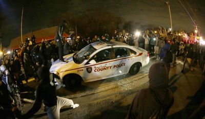 FILE - In this Nov. 24, 2014, file photo, a protester squirts lighter fluid on the police car as the car windows are shattered near the Ferguson Police Department after the announcement of the grand jury decision in Ferguson, Mo, deciding not to indict Ferguson police officer Darren Wilson in the death of Michael Brown, the unarmed, black 18-year-old whose fatal shooting sparked sometimes violent protests. Attorneys for the U.S. Department of Justice say Ferguson, Missouri, is making progress in the effort to end racial bias in police and court practices, but more transparency is needed. U.S. District Judge Catherine Perry on Thursday, June 22, 2017, heard an update on a consent agreement reached in 2016.(AP Photo/Charlie Riedel, File)