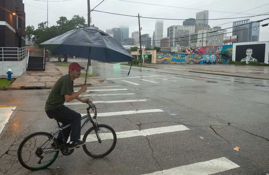 A man shields himself from the rain while riding his bicycle on the intersection of St. Emmanuel and Leeland streets Thursday, June 22, 2017, in Houston as Tropical Storm Cindy hit Southeast Texas and the Gulf Coast. (Godofredo A. Vasquez/Houston Chronicle via AP)
