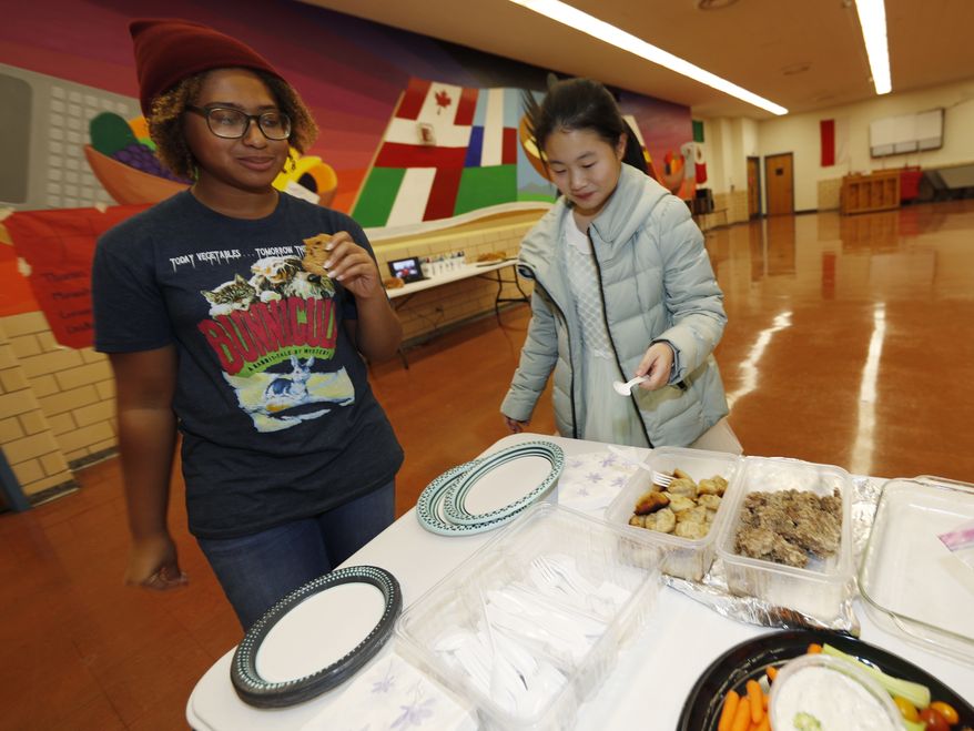 In this Jan. 27, 2017 photo, Thandi Glick looks on as the foreign exchange student that her family is hosting, Miaofan Chen, begins her way through the serving line during a potluck meal for Chinese exchange students and their families at a school in Denver. For many American families, hosting a foreign student is a way to bring other cultures to their doorsteps without ever leaving home. (AP Photo/David Zalubowski)