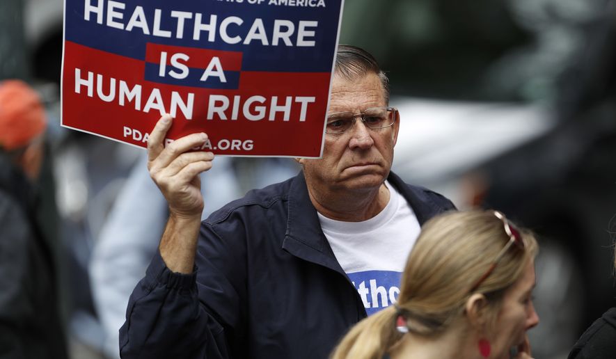 A protester waves a placard during a rally, Friday, June 23, 2017, in downtown Denver, against the Republican health bill that was recently unveiled in the U.S. Senate. More than 100 protesters crowded the sidewalk outside the building in which U.S. Sen. Cory Gardner, R-Colo., has his office. (AP Photo/David Zalubowski)