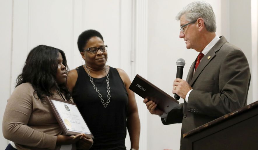 Mississippi Republican Gov. Phil Bryant, right, reads the citation as he honors Tausha Rawls, left, and Melody Vaughn, two Mississippi Department of Child Protection Services social workers for their actions which saved the life of a Madison County child earlier this year, with the first ever Governor's Award for Outstanding Service in Child Protection and Well-Being during a statewide meeting of MDCPS social workers in Jackson, Miss., Friday, June 23, 2017. (AP Photo/Rogelio V. Solis)