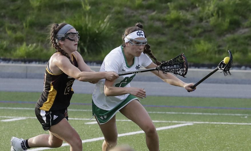 In this May, 3, 2017 photo, Mercy's Libby Bartels, left, reaches in on Cranbrook Kingswood's Angelina Wiater during a lacrosse game at Cranbrook Kingswood School in Bloomfield Hills, Mich. Helmets are not a required piece of equipment worn by female high school lacrosse players. And this year, the National Federation of State High School Associations allowed the optional use of two models of headgear beyond the previously allowed padded headbands. (AP Photo/Carlos Osorio)