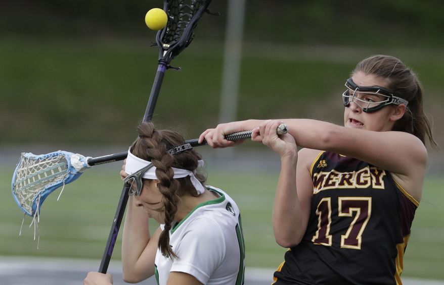 In this May, 3, 2017 photo, Mercy's Grace Canty (17) hits the stick of Cranbrook Kingswood's Angelina Wiater during a lacrosse game at the Cranbrook Kingswood School in Bloomfield Hills, Mich. Helmets are not a required piece of equipment worn by female high school lacrosse players. And this year, the National Federation of State High School Associations allowed the optional use of two models of headgear beyond the previously allowed padded headbands. In 2018, Florida will become the first state to mandate high school female lacrosse players wear protective equipment over their entire head. (AP Photo/Carlos Osorio)