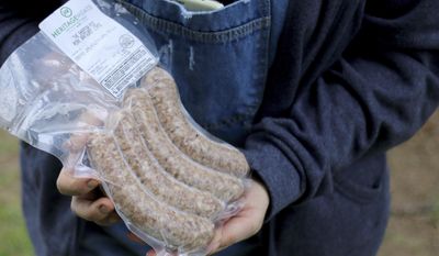 In this Tuesday, June 13, 2017 photo, Tania Issa holds a package of the sheepish pig pork bratwurst links that are made from the mangalitsa pigs she raises at her farm in Kingston, Wash.  (Michaela Roman/Kitsap Sun via AP)
