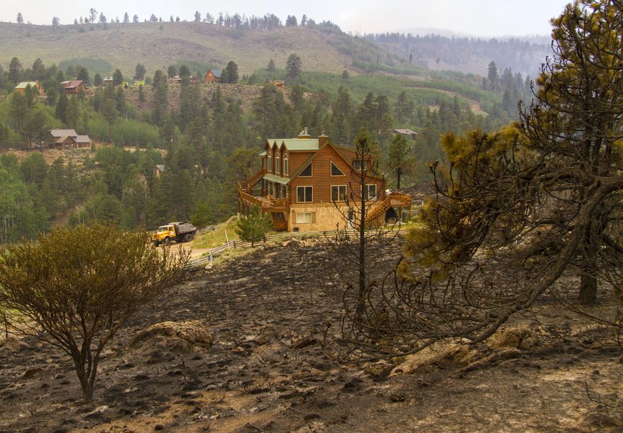 This Saturday, June 24, 2017, photo, shows a home near a burnt hillside caused by a wildfire fire on the west side of Panguitch Lake, near Panguitch, Utah. Nearly 1,000 firefighters battled a Utah wildfire that grew Sunday morning that has prompted the evacuation of over a 1,000 people from hundreds of homes and cabins. (Jordan Allred/The Spectrum via AP)