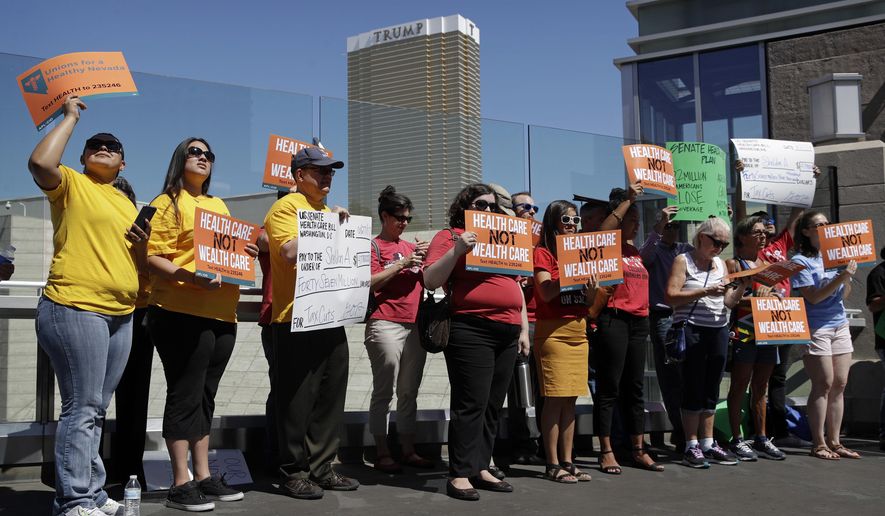 People protest with the Trump International hotel in the background, Tuesday, June 27, 2017, in Las Vegas. Union officials in Nevada, community members and others gathered Tuesday at a pedestrian bridge over the Las Vegas Strip to urge Republican U.S. Sen. Dean Heller to continue to oppose the current GOP health care bill. (AP Photo/John Locher)