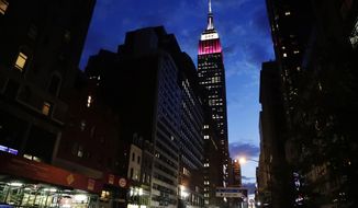 In this Tuesday, June 27, 2017 photo, pedestrians navigate 34th street as the Empire State Building in New York City is lit up in burgundy and white for Qatar Airways in New York. The top of the Empire State Building was lit in the airlines&#39; colors Tuesday night to recognize its 10th anniversary of flying to the United States. (AP Photo/Frank Franklin II)