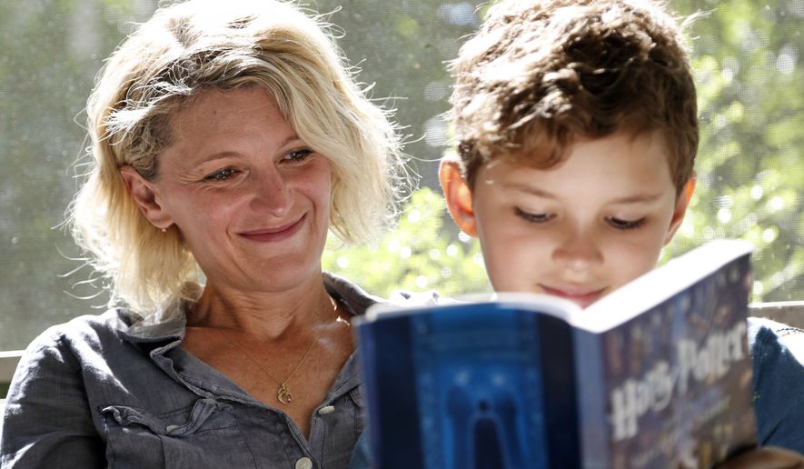 Theo Galkin, 8, rereads a favorite part of "Harry Potter and the Sorcerer's Stone" while posing for a picture with his mother Chloe Galkin at their home in South Orange, N.J., Wednesday, June 28, 2017. As the 20th anniversary of the initial publishing of the first Harry Potter book is celebrated this week, another generation is being introduced to Harry, Hogwarts and all the rest of the magical world created by author J.K. Rowling. (AP Photo/Seth Wenig)