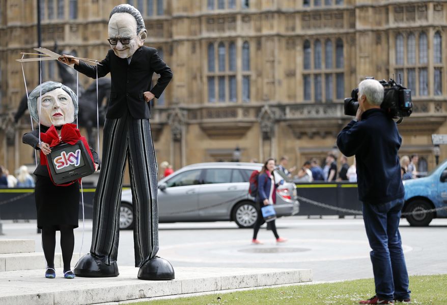 A camera man films campaigners from the community-based organization Avaaz, wearing a mask of Rupert Murdoch, centre right, and Prime Minister Theresa May, stage a protest opposite parliament in London, Thursday, June 29, 2017. Britain’s Culture Secretary Karen Bradley is ruling on whether to permit the proposed 11.7 billion pound merge of Sky and Twenty-First Century Fox. Bradley is set to offer her verdict Thursday. The merger would allow Rupert Murdoch to consolidate his power base in British media. (AP Photo/Frank Augstein)