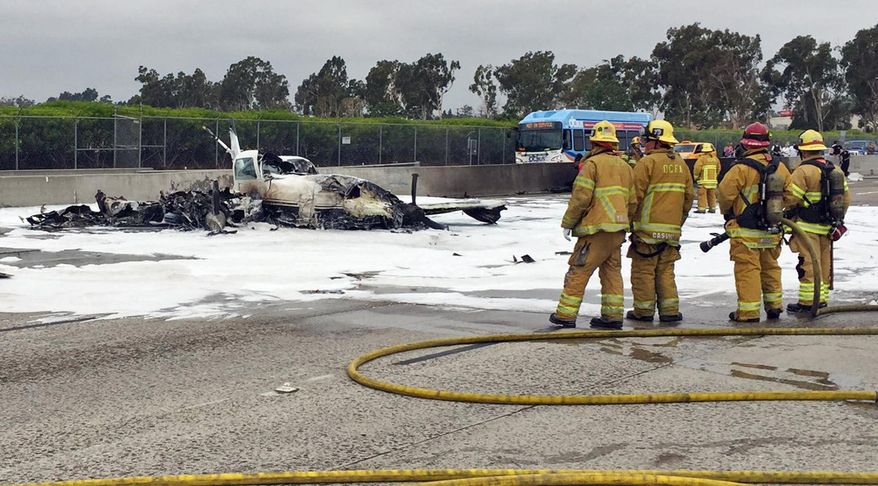 This photo provided by the Orange County Fire Authority shows firefighters standing by the wreckage of a twin-engine prop jet after it crashed on Interstate 405, just short of the runway at John Wayne Orange County Airport, in Costa Mesa, Calif., Friday, June 30, 2017. Officials said two people were injured and were taken by helicopter to a hospital. The freeway was shut down in both directions. (Orange County Fire Authority via AP)