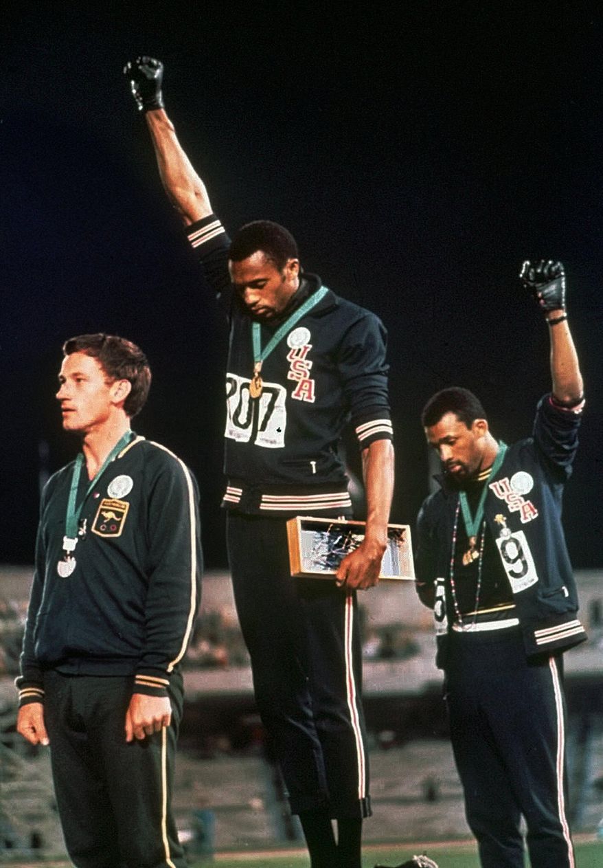FILE - In this Oct. 16, 1968, file photo, extending gloved hands skyward in racial protest, U.S. athletes Tommie Smith, center, and John Carlos stare downward during the playing of "The Star-Spangled Banner" after Smith received the gold and Carlos the bronze medal in the 200 meter run at the Summer Olympic Games in Mexico City. Australian silver medalist Peter Norman is at left. Smith and Carlos each wore a black glove and raised a fist in the air during the medal ceremony as a sign of solidarity with those fighting for greater equality, which some dubbed as radical and an endorsement of the black power movement. (AP Photo/File)