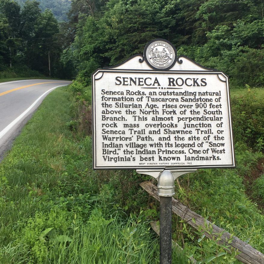 In this June 25, 2017 photo a sign at the edge of Seneca Rocks in eastern West Virginia, between the hamlet's general store/restaurants and its climbing cliff, describes some of its natural and human history. (AP Photo/Michael Virtanen)
