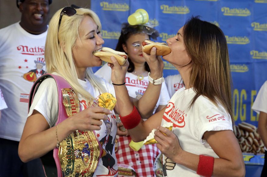 Current women&#39;s champion Miki Sudo, left, of Las Vegas, and challenger Michelle Lesco, of Tuscon, Ariz., feed each other a hot dog Monday, July 3, 2017, during the weigh-in for the 2017 Nathan&#39;s Hot Dog Eating Contest, in Brooklyn Borough Hall, in New York. Ms. Suto weighed-in at 126 pounds, while Ms. Lesco tipped the scales at 104.5 pounds.(AP Photo/Richard Drew)