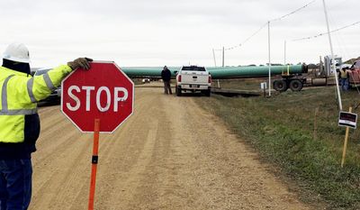 FILE - In t his Oct. 11, 2016, file photo, a crew member stops traffic as work resumed on the four-state Dakota Access pipeline near St. Anthony, N.D. A dispute over whether Energy Transfer Partners the developer of the $3.8 billion Dakota Access pipeline improperly reported the discovery of American Indian artifacts in North Dakota will linger into fall 2017. Energy Transfer Partners has been battling since state regulators filed a November complaint and proposed a $15,000 fine. A public hearing on the issue that was scheduled Aug. 16, 2017, is being delayed so attorneys can first make written arguments. (AP Photo/Blake Nicholson, File)